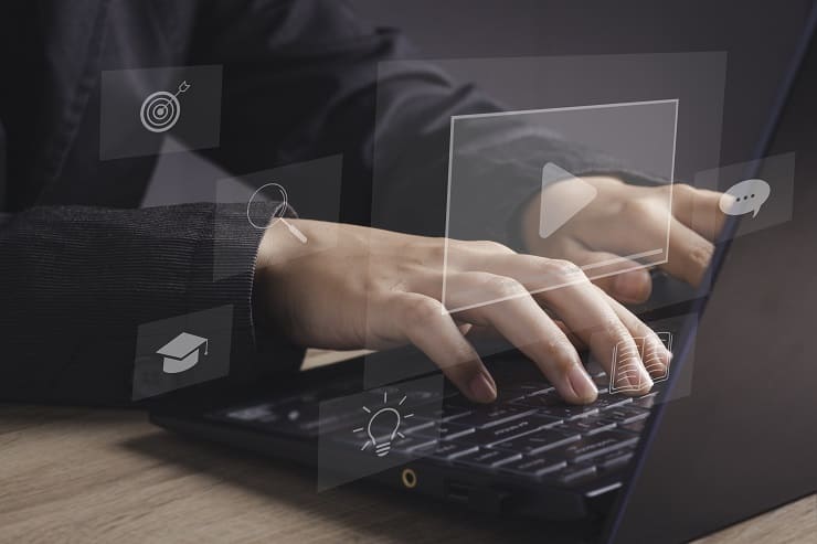 E-Learning: Hände tippen auf Laptop mit eingeblendeten digitalen Icons