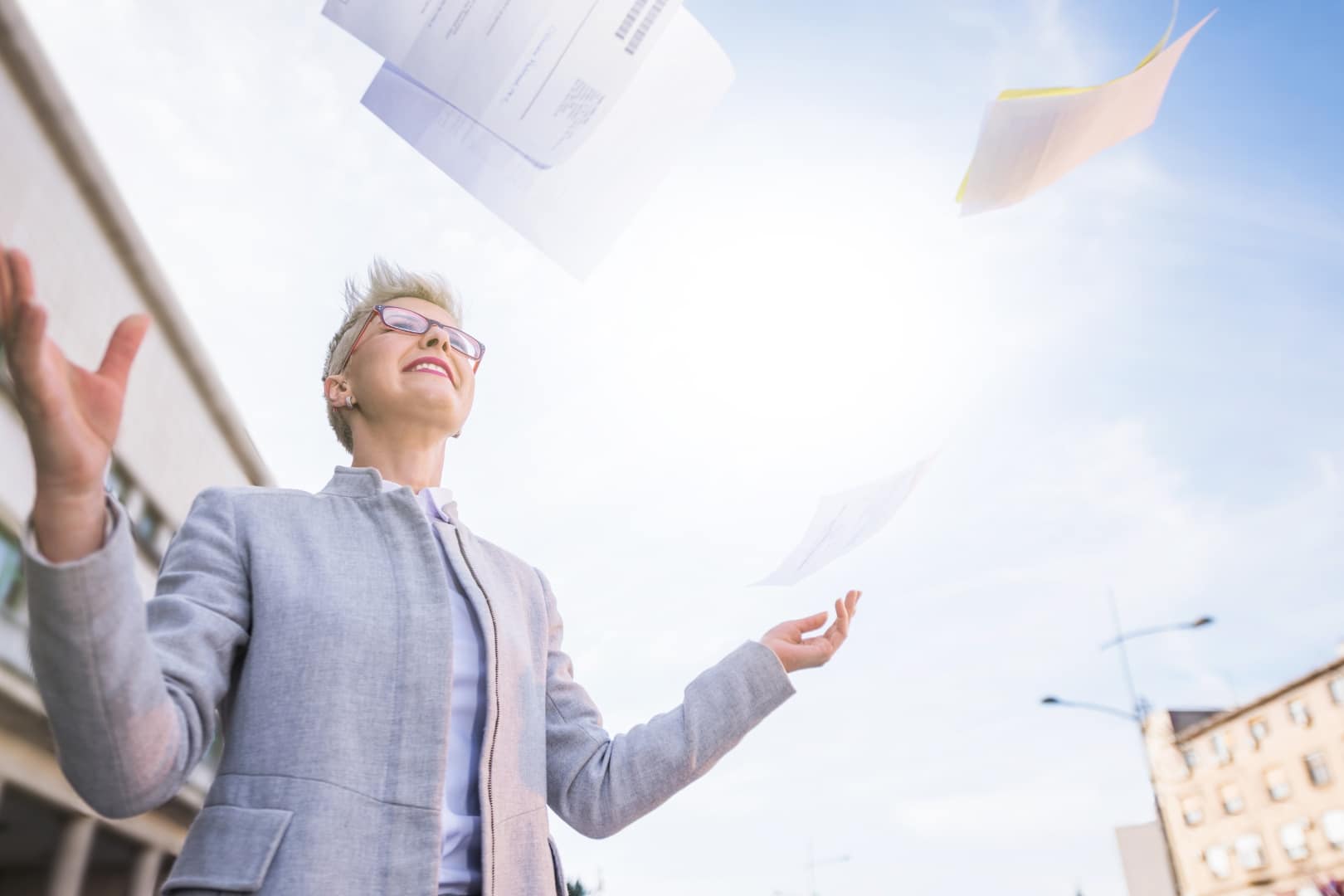 Payroll Service: Geschäftsfrau wirft Papierdokumente in die Luft als Symbol für digitale Prozesse und papierloses Arbeiten